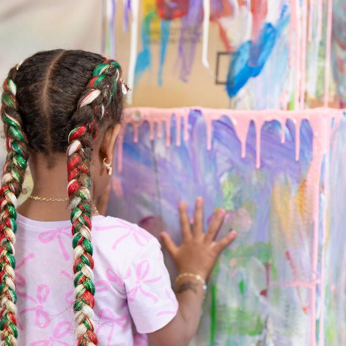 Child with braided hair interacting with a colorful art installation.