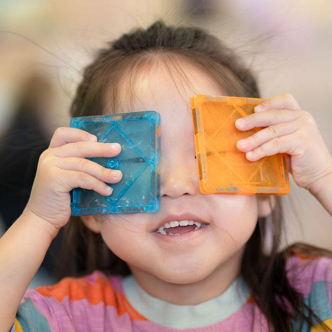 Child holding colorful geometric shapes over their eyes with a blurred background