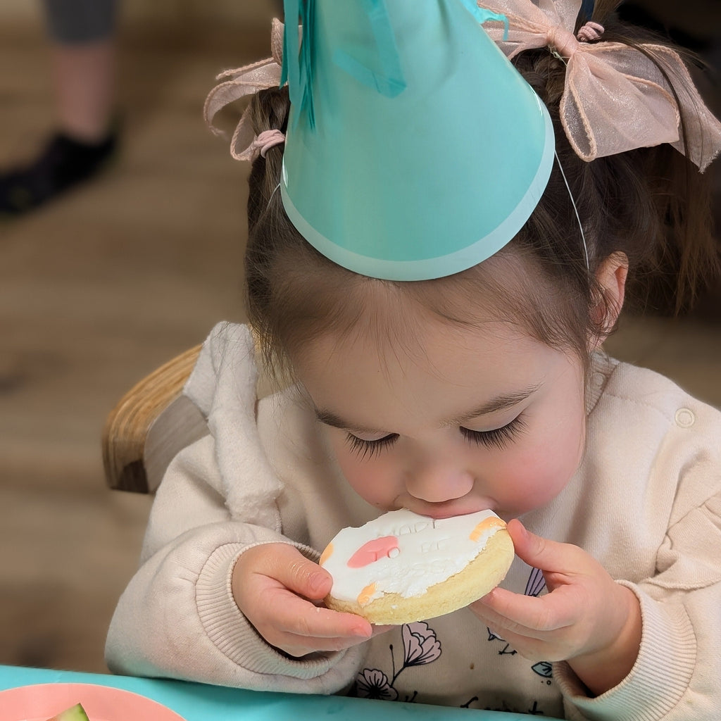 Child wearing a blue party hat eating a cookie at a table with watermelon slices.